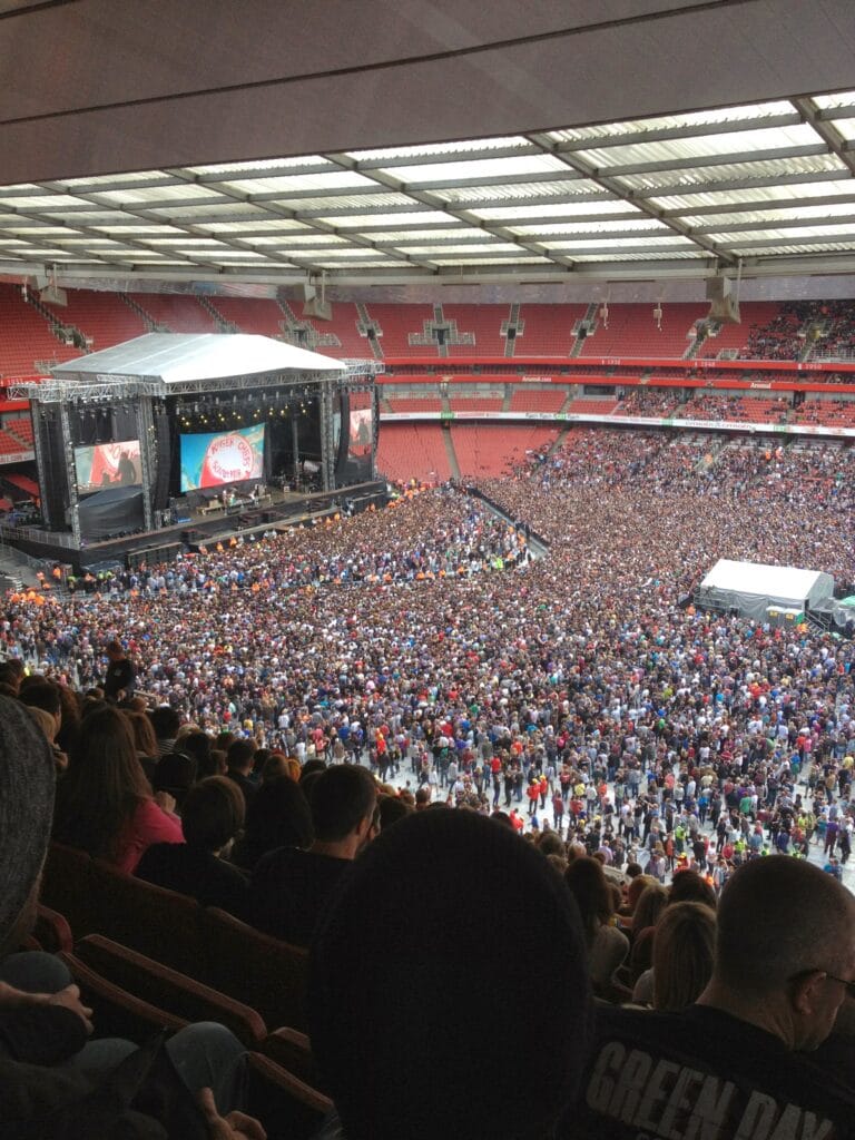 Picture of a crowd of people at The Emirates Stadium in London with a stage and the band Green Day playing