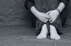 Black and white photo of womens legs sat down with hands folded